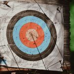 Detailed photo of a colorful archery target filled with arrows, indicating multiple hits. Outdoors daylight shot.